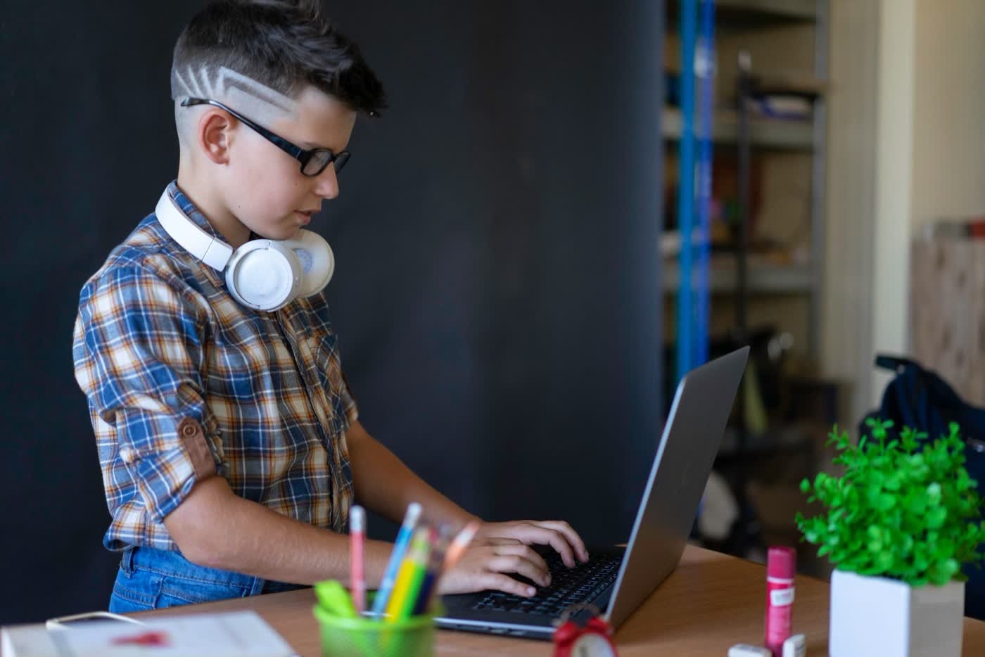 Enfant qui suit un cours de code en ligne depuis la maison, casque autour du cou